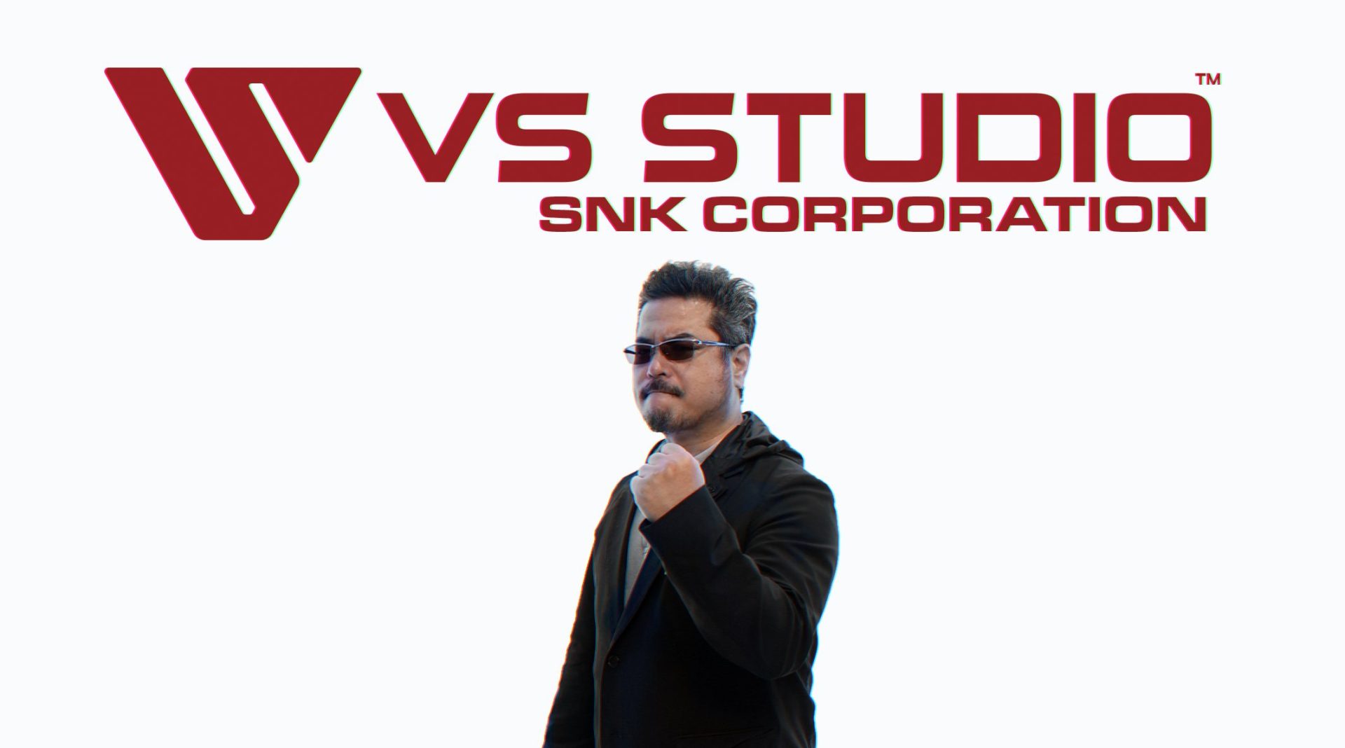 Katsuhiro Harada standing in front of the VS Studio SNK Corporation logo with his fist raised